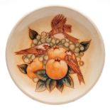A John Moorcroft pottery plate, tube lined in the Finches pattern on a peach ground,