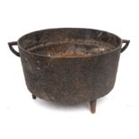 An iron circular open cooking pot with twin angular handles and tripod feet, 28cm diameter,
