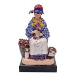 A Harry Parr pottery figure of a flower seller modelled as a girl seated on a large basket and