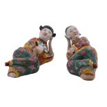 A pair of Chinese porcelain figures of a reclining male and female figure attired in colourful