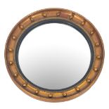 A giltwood and gesso circular convex wall mirror in the Regency taste, the plate within an ebonised,