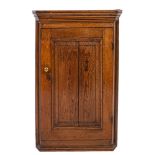 A George III oak hanging corner cupboard, circa 1800; with moulded cornice above a panel door,