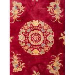 A Chinese carpet, 20th century; machine woven, with a central floral medallion on a cerise ground,