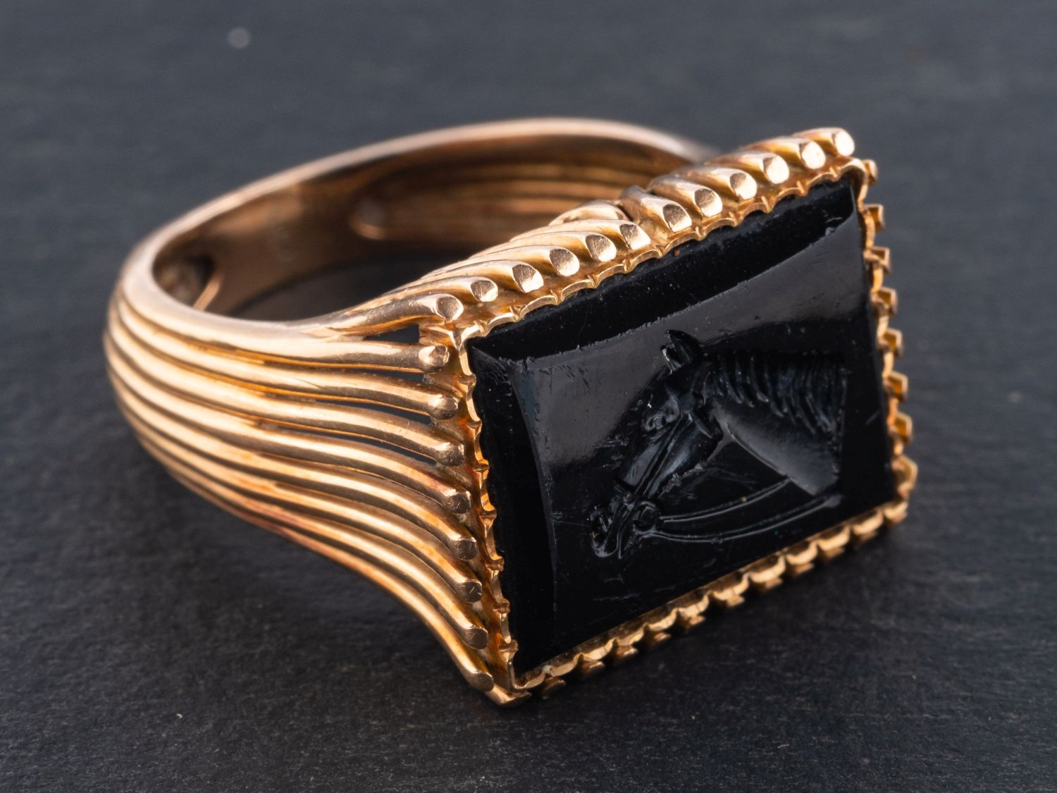 An black paste intaglio ring, depicting a horse's head, with reeded shoulders and mount,