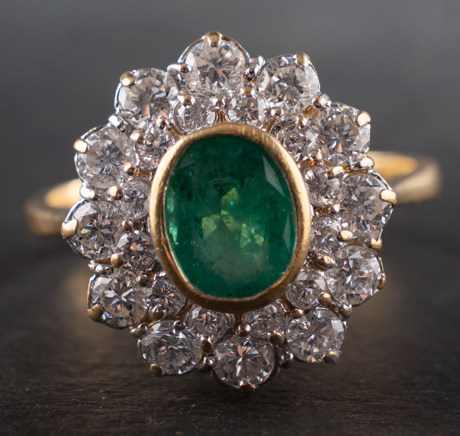 An 18ct gold, oval, mixed-cut emerald and round, brilliant-cut diamond cluster ring,