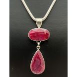 A modern design drop style silver pendant set with an oval cut and a teardrop cut ruby. On a 16 inch