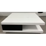 A modern black and white square shaped low coffee table with gloss finish. with 2 black drawers