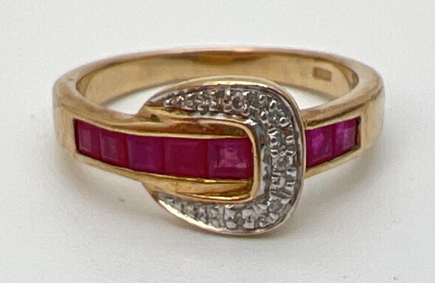 A 9ct gold ruby and diamond set buckle style dress ring. Band channel set with 5 square cut