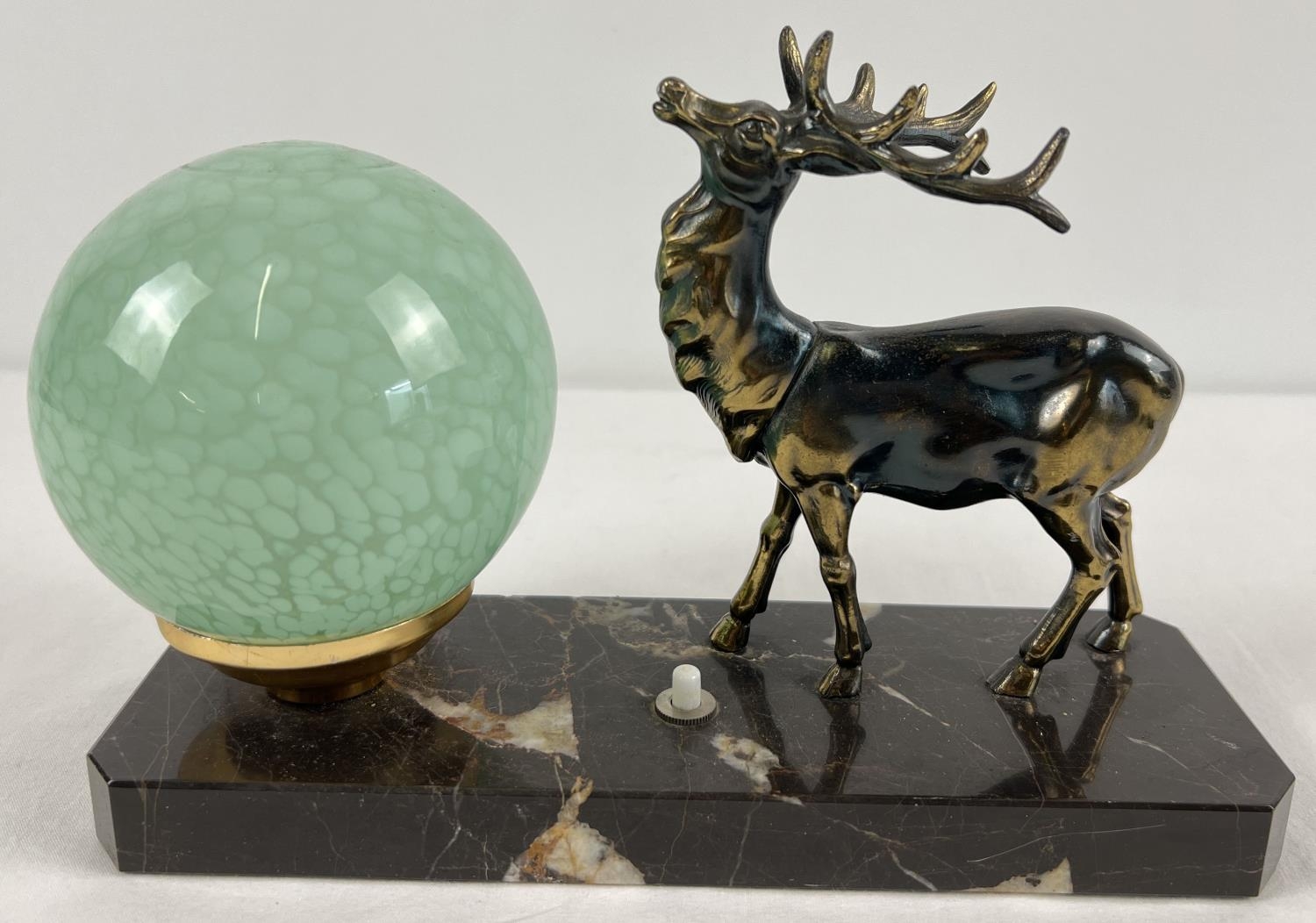 An Art Deco design table lamp with spelter figure of a stag and spherical green glass shade. On a