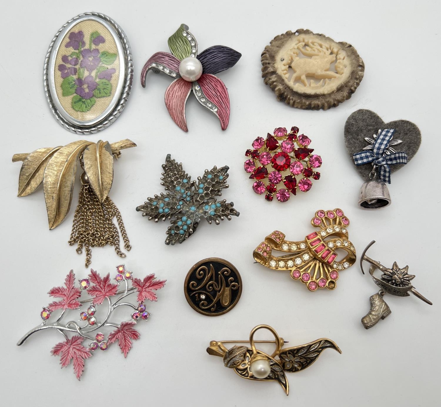 A collection of 12 vintage brooches in various designs, mostly floral and alpine themed. To