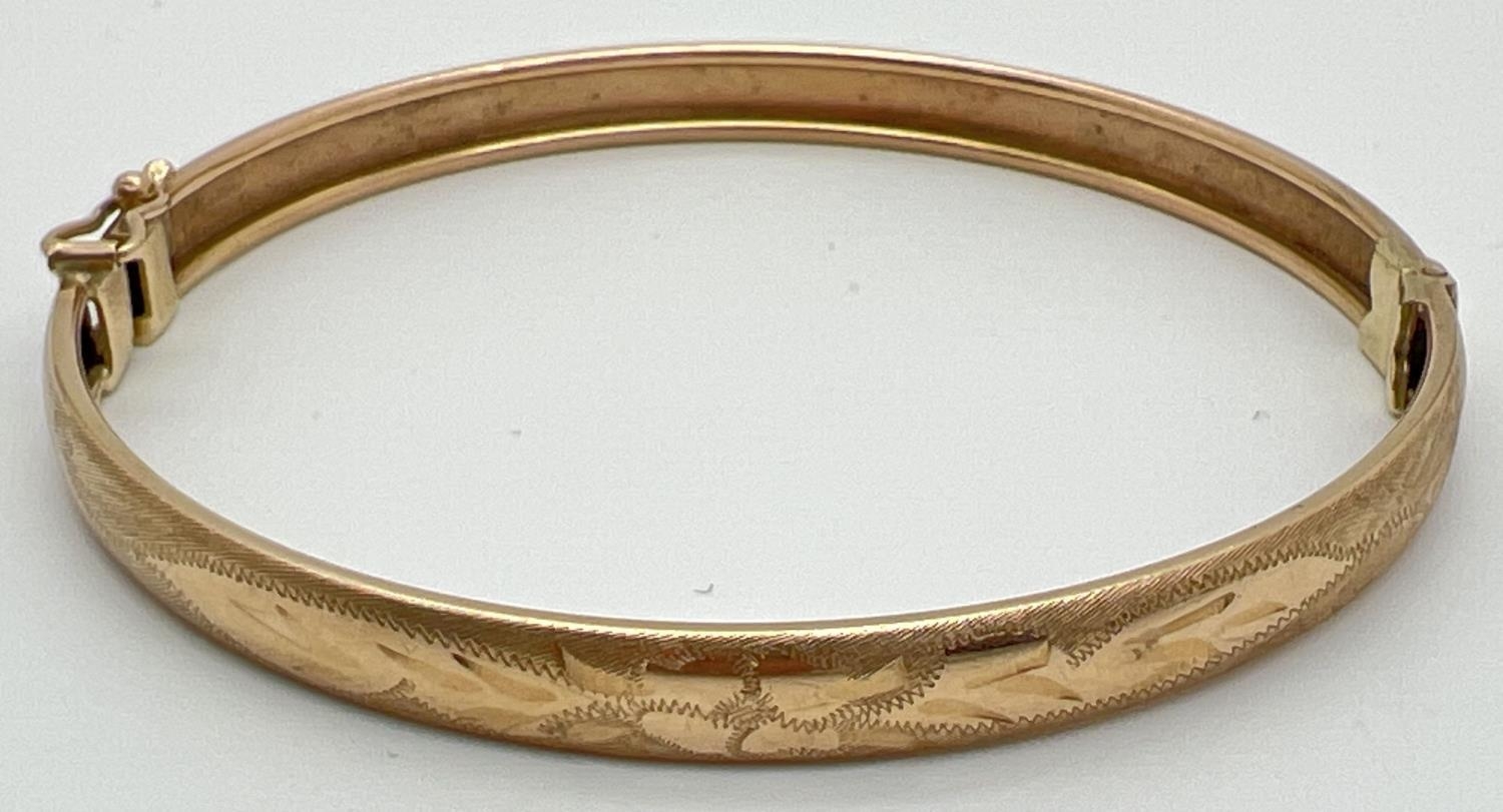 A vintage 9ct gold bangle with half floral engraving and safety clip (in need of attention) to