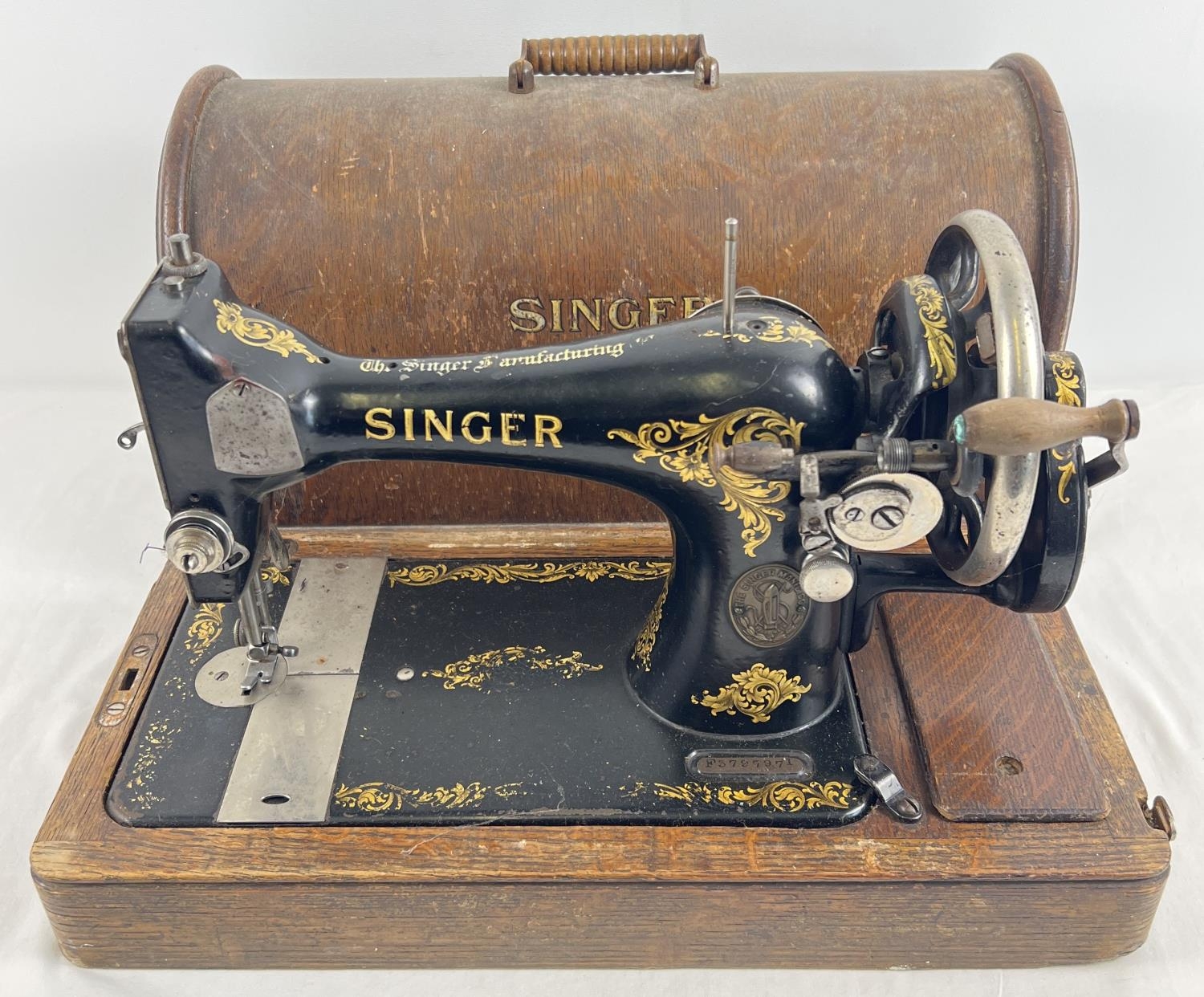 An antique wooden cased Singer sewing machine, black with gold floral decoration and shuttle bobbin.