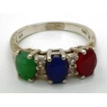 A silver trilogy dress ring set with oval cut emerald, sapphire & ruby interspersed with 4 small