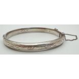 A vintage silver bangle with half floral engraved detail and safety chain. Inscription to inside