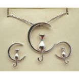 A silver pendant necklace and matching stud earrings of a cat sitting on a crescent moon. Pendant is
