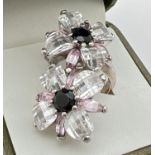 A large white metal double flower head design cocktail ring. Set with faceted black stones and