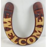 A cast iron Welcome wall plaque in the shape of a horseshoe, with gold painted lettering. Approx.
