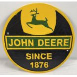 A circular shaped John Deere wall plaque, painted in green, black and yellow. With holes for fixing.