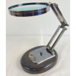 A large desk top magnifying glass, mounted on a wooden base, with adjustable metal stand. Glass