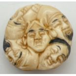 A carved Chinese circular shaped netsuke depicting many faces to both sides. With signature mark.