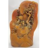 A large carved Chinese yellow/orange coloured boulder depicting figures, trees and houses on a