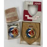 A vintage boxed car badge and fixings, together with a matching wooden heraldic shield. Although