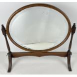 An antique dark wood framed, oval shaped, bevel edged swing mirror on stand. With brass fixings.