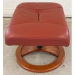 A modern Verikon rust coloured leather topped sloped footstool with circular shaped wooden base.