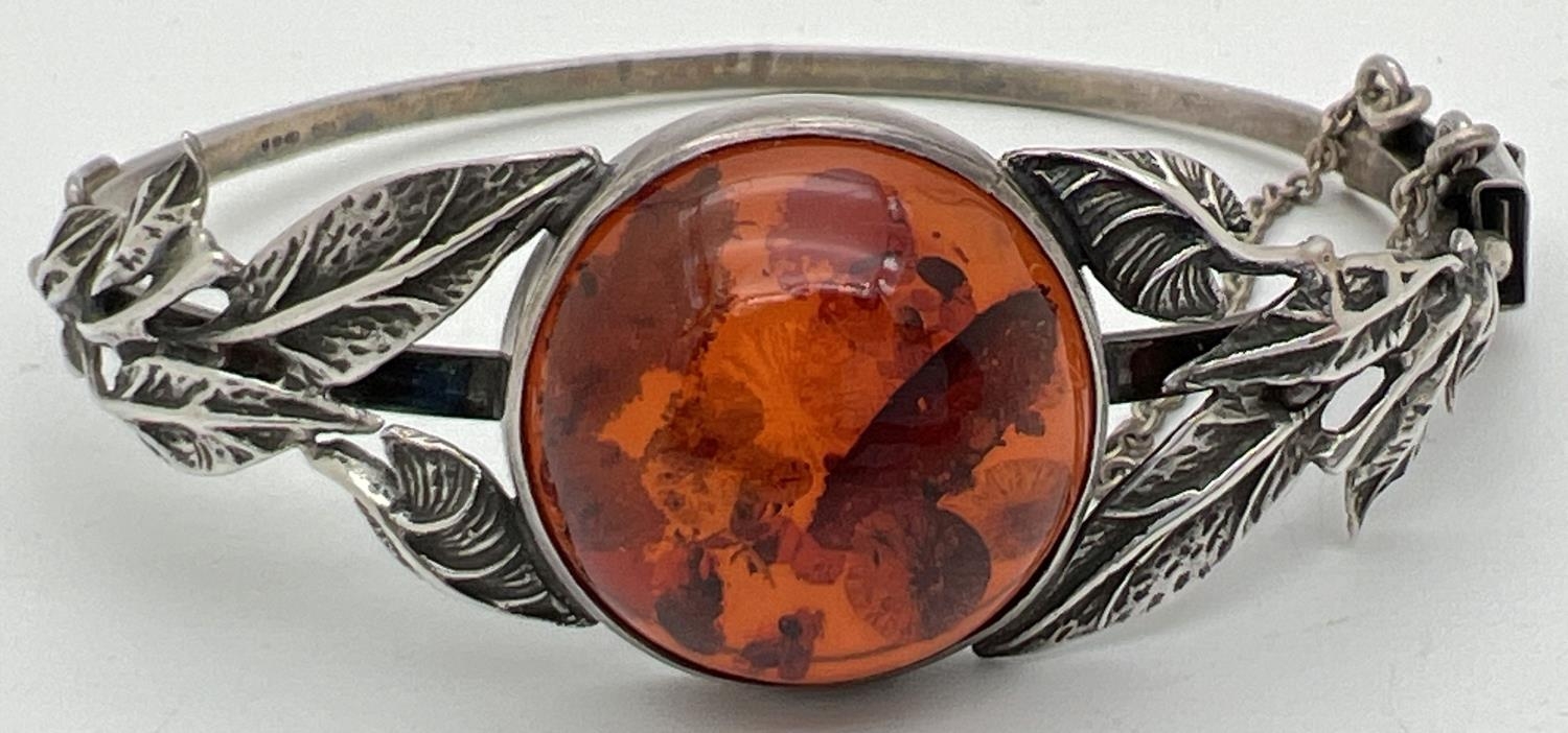 A silver bangle style bracelet set with a round cut piece of cognac amber with leaf design to both