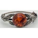 A silver bangle style bracelet set with a round cut piece of cognac amber with leaf design to both