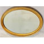 A large oval shaped gilt framed wall mirror with bevel edged glass. Approx. 61cm x 91cm.