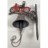 A wall mountable painted cast iron garden bell with painted motorcyclist detail and leather strap
