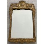 A vintage gilt framed wall hanging mirror with ornate detail to top. Approx. 63cm tall x 40cm wide.