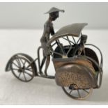A small brass model of a rickshaw with hammered detail to mudguards and shade and moving rear wheel.