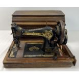 A vintage Singer hand crank sewing machine, in wooden case. Painted black with gilt floral
