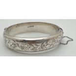 A vintage silver bangle with floral design engraving throughout, push clasp and safety chain. 1.5 cm