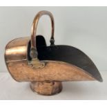 A Victorian copper and brass helmet fireside coal scuttle with hinged swing handle. Raised on a