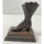 A vintage cast metal figure of a Victorian boot screwed onto a stepped base with remnants of