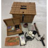 A wicker fishing basket with carry strap containing a collection of fishing accessories. To