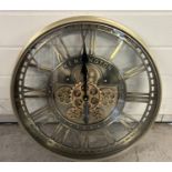 A very large modern brushed bronzed metal wall clock with glass face, roman numeral markers & cog