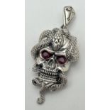 An unmarked white metal pendant in the form of a skull with a snake, set with rubies for eyes.