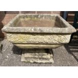 A large square shaped 2 sectional concrete garden planter with pedestal base and rose design border.