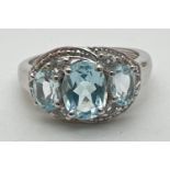 A silver and topaz trilogy dress ring, set with 3 oval cut blue topaz stones in an illusion halo