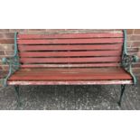 A wooden slatted garden bench with cast iron ends, painted green. Bench ends have floral & lions