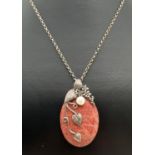 A natural red stone oval shaped pendant with silver floral design overlay, set with a single