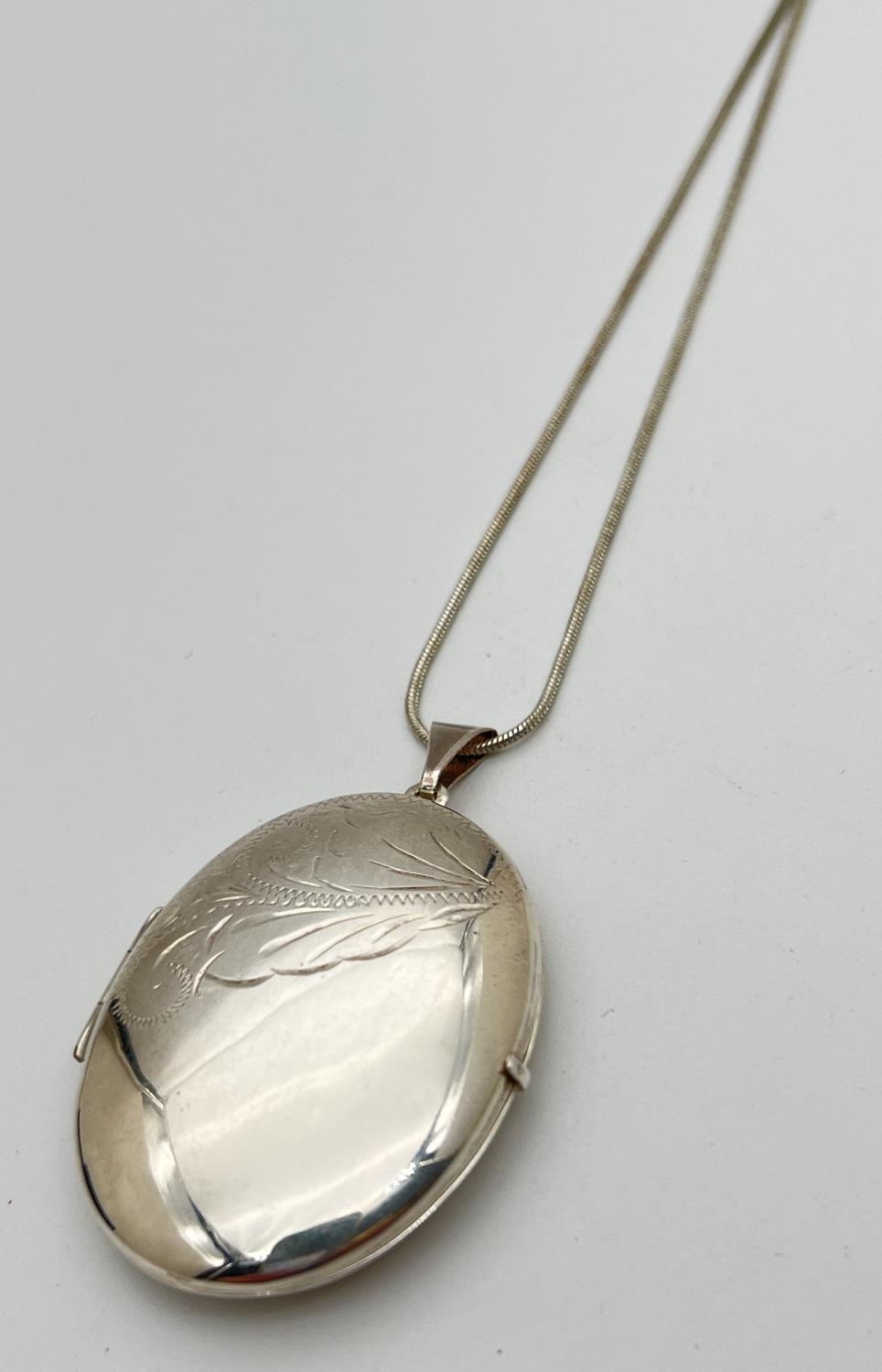 A large silver oval locket with engraved floral design to front. On a 22" snake chain with lobster