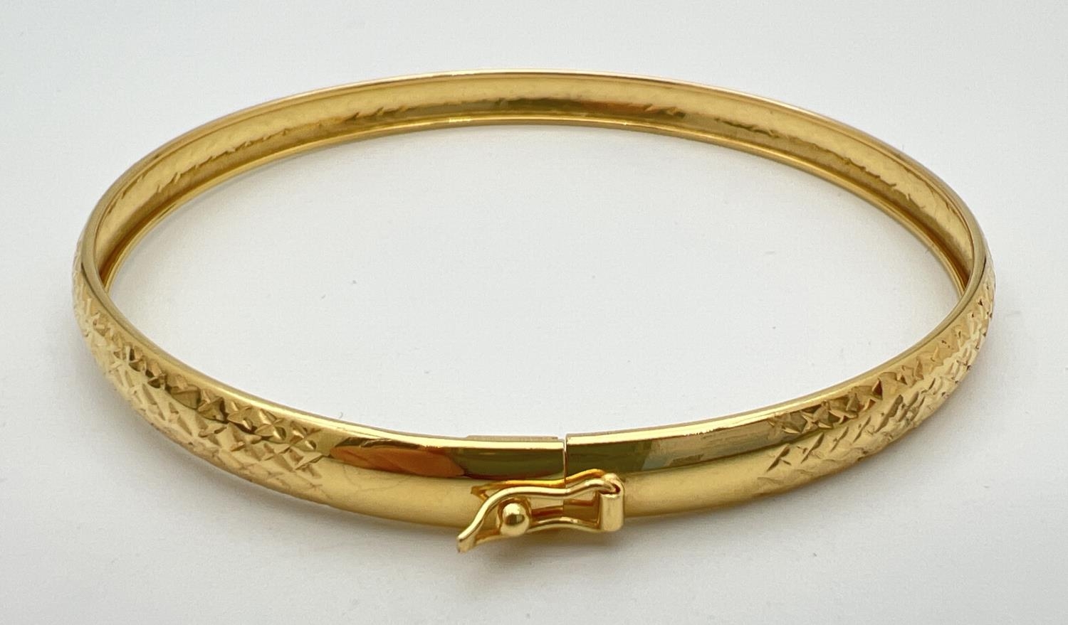 A silver gilt bangle with diamond cut criss cross pattern throughout. Push clasp and safety clip.