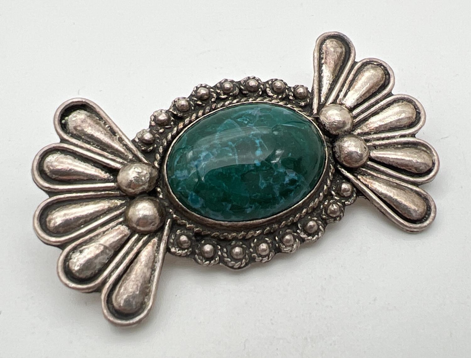 A silver modern design Floral style brooch set with a central oval green stone. Silver mark to back.