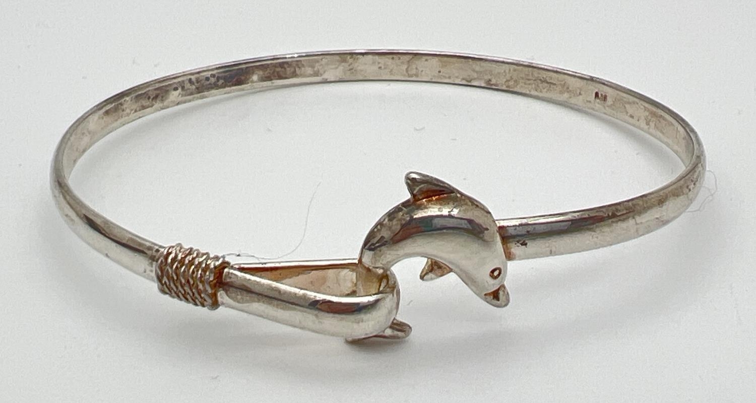 A 925 silver bangle with dolphin detail. Tail of dolphin hooks into loop clasp to secure bracelet.