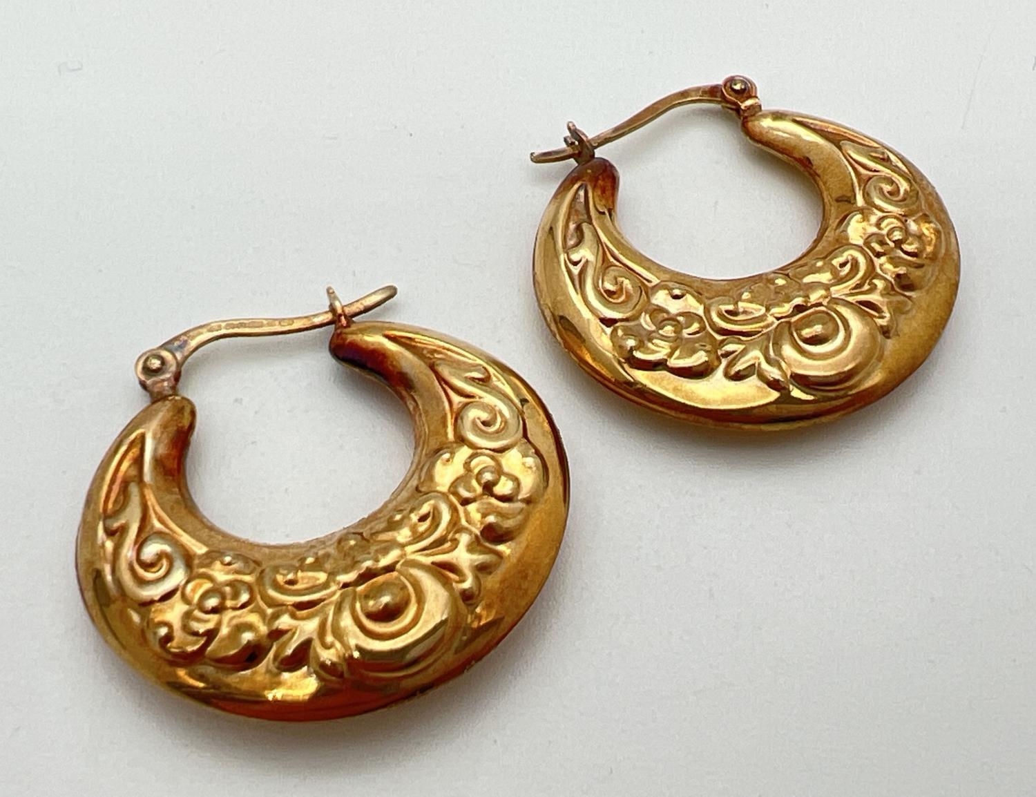 A pair of 9ct gold creole style earrings with floral pattern and hinged posts. Approx. 2.75cm